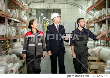 Two young engineers in workwear and mature director of factory in formalwear 70324763