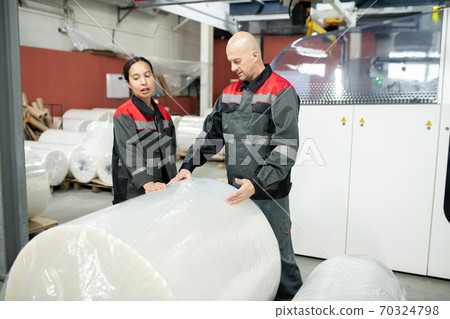 Young female factory worker and her male colleague standing by huge packed roll 70324798