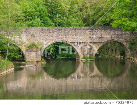 An old stone bridge reflected in the water 70324975