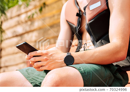 Hands of young active man in safety jacket and shorts scrolling in mobile phone 70324996