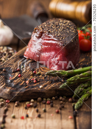 Slice of Raw Beef Topside Joint with Salt and Pepper on wooden chopping board with tomatoes garlic  70326293