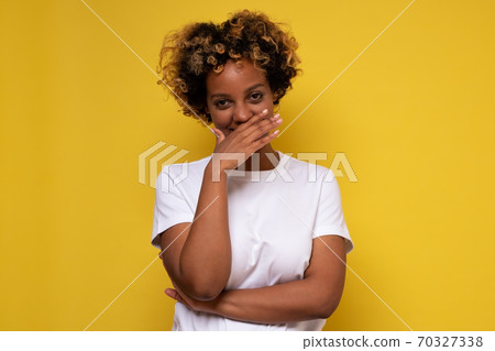 Young african woman giggles covering her mouth with hand, hiding her emotion Young african woman giggles covering her mouth with hand, hiding her emotion 70327338