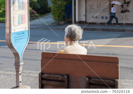 Grandmother sitting on the bench and waiting for the bus 70328116