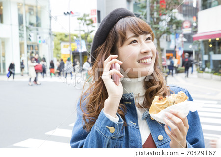 A woman eating Taiyaki while calling A woman eating Taiyaki while calling 70329167