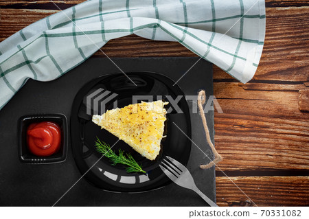 piece of omelet on black plate with ketchup. piece of omelet on black plate with ketchup. 70331082