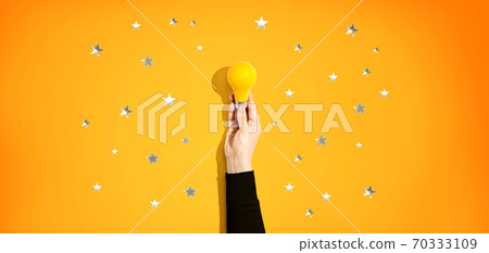 Person holding a yellow light bulb with stars Person holding a yellow light bulb with stars 70333109