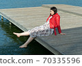 young beautiful woman sits on a bridge by the lake, legs down, sits in a red jacket 70335596