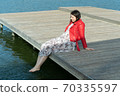 young beautiful woman sits on a bridge by the lake, legs down, sits in a red jacket 70335597