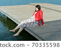 young beautiful woman sits on a bridge by the lake, legs down, sits in a red jacket 70335598