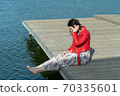young beautiful woman sits on a bridge by the lake, legs down, sits in a red jacket 70335601