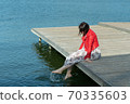 young beautiful woman sits on a bridge by the lake, legs down, sits in a red jacket 70335603