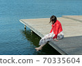 young beautiful woman sits on a bridge by the lake, legs down, sits in a red jacket 70335604