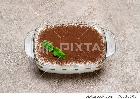 Traditional Italian Tiramisu dessert in glass baking dish on concrete background Traditional Italian Tiramisu dessert in glass baking dish on concrete background 70336505