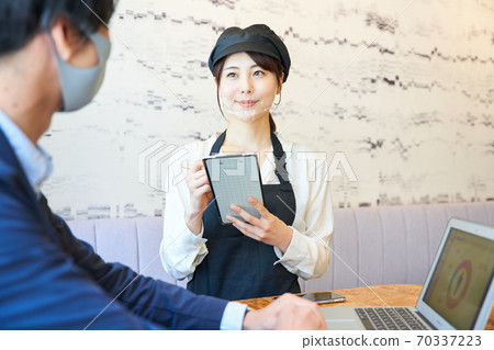 A woman wearing a transparent mask and taking an order at a cafe 70337223