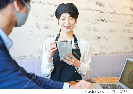 A woman wearing a transparent mask and taking an order at a cafe 70337224