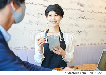 A woman wearing a transparent mask and taking an order at a cafe 70337225