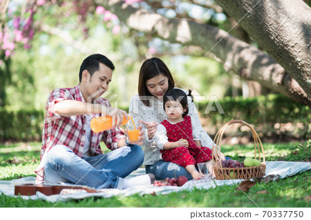 Happy family sitting on the grass during a picnic in a park Happy family sitting on the grass during a picnic in a park 70337750