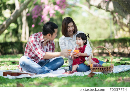 Happy family sitting on the grass during a picnic in a park Happy family sitting on the grass during a picnic in a park 70337754