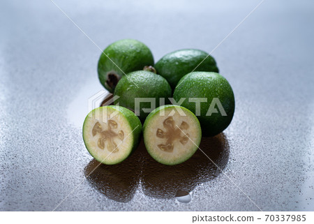 Still life of feijoa fruits on a damp reflective surface. In the foreground, the cut fruit is turned inside. Background. 70337985