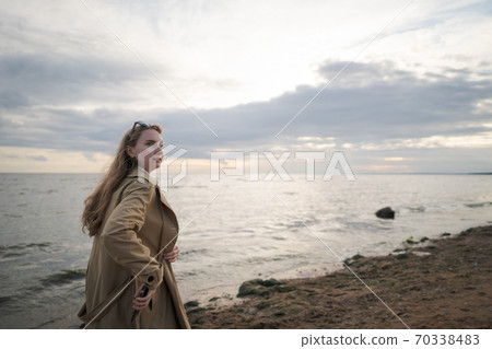 pretty girl walking on a beach in beige trench coat with warm evening light 70338483
