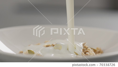 pour yogurt over granola with almond flakes and pumpkin seeds into white bowl closeup 70338726