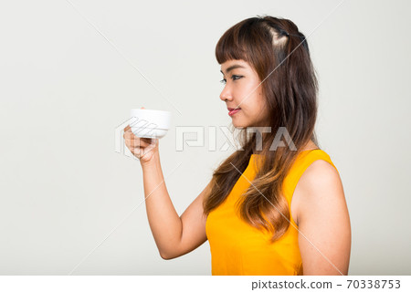 Profile view of young beautiful Asian woman holding coffee cup Profile view of young beautiful Asian woman holding coffee cup 70338753