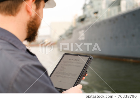 Navigation officer reading contract on tablet near vessel in background. 70338790