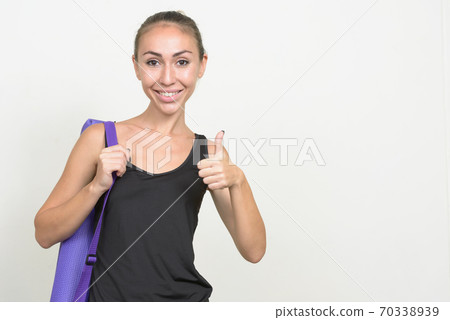 Portrait of happy young woman with yoga mat giving thumbs up and ready for gym Portrait of happy young woman with yoga mat giving thumbs up and ready for gym 70338939