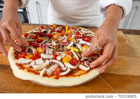 A view of the hands of the chef adding hot peppers to the pizza toppings. Vegan food. 70339805