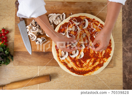 Close-up on the hands of a cook laying mushrooms on a pizza. View from above. Vegan food. 70339828