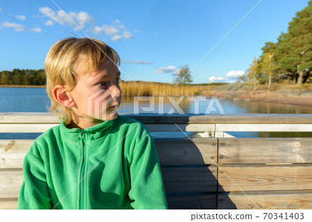 Profile view of young handsome boy thinking at wooden pier Profile view of young handsome boy thinking at wooden pier 70341403