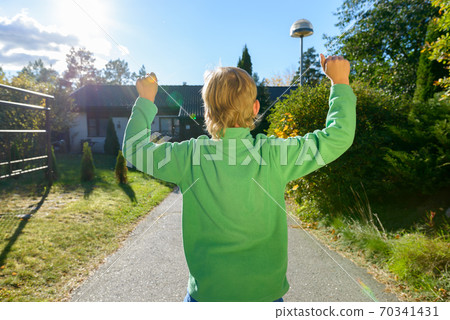 Rear view of happy young boy with fists raised in the front yard 70341431