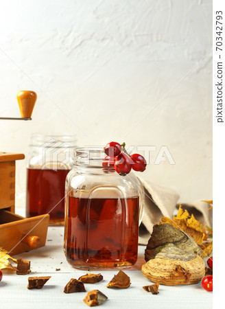 A glass Cup with a hot drink made of rosehip and wood mushroom on a light table with ingredients for cooking. Vertically, with space 70342793