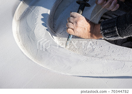 Closeup of an artist carving curves into a white stone 70344782