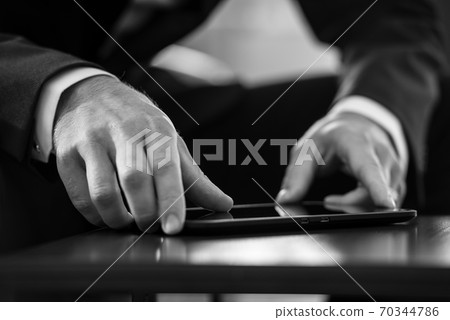 Businessman sitting at black table navigating a tablet computer 70344786