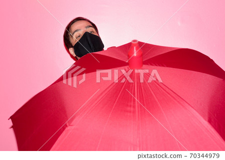 Persian businessman with mask holding umbrella against pink wall Persian businessman with mask holding umbrella against pink wall 70344979