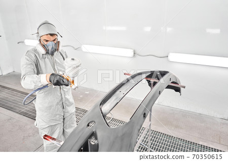 Worker painting parts of the car in special painting chamber, wearing costume and protective gear. Car service station. Worker painting parts of the car in special painting chamber, wearing costume and protective gear. Car service station. 70350615