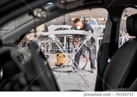 The mechanic works with a grinding tool. Sanding of car elements. Garage painting car service. Repairing car section after the accident. 70350715