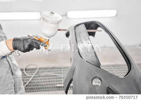 Worker painting parts of the car in special painting chamber, wearing costume and protective gear. Car service station. Worker painting parts of the car in special painting chamber, wearing costume and protective gear. Car service station. 70350717