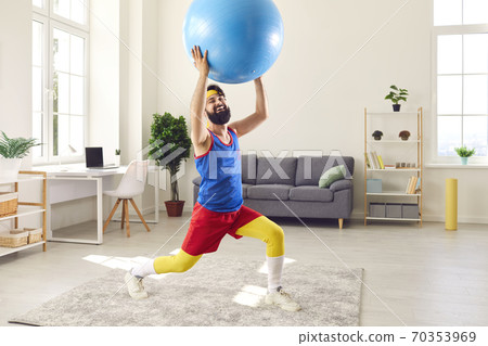 Cheerful bearded man in colorful sportswear doing sports workout with fitness ball at home 70353969
