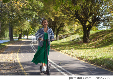 Happy woman riding on an e-scooter. Young and beautiful caucasian woman rides electric scooter in 70357729