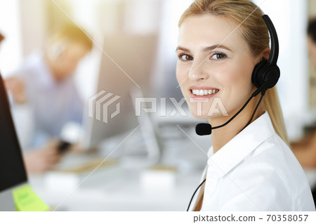 Blond business woman using headset for communication and consulting people at sunny office. Call center Blond business woman using headset for communication and consulting people at sunny office. Call center 70358057
