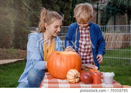 A boy and his mother cut a pumpkin. A young mother and son are preparing a pumpkin for Halloween. Preparing for Halloween. Peel an orange pumpkin. A boy and his mother cut a pumpkin. A young mother and son are preparing a pumpkin for Halloween. Preparing for Halloween. Peel an orange pumpkin. 70358795