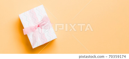 wrapped Christmas or other holiday handmade present in paper with pink ribbon on orange background. Present box, decoration of gift on colored table, top view with copy space wrapped Christmas or other holiday handmade present in paper with pink ribbon on orange background. Present box, decoration of gift on colored table, top view with copy space 70359174