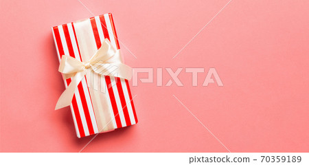 wrapped Christmas or other holiday handmade present in paper with yellow ribbon on living coral background. Present box, decoration of gift on colored table, top view with copy space wrapped Christmas or other holiday handmade present in paper with yellow ribbon on living coral background. Present box, decoration of gift on colored table, top view with copy space 70359189