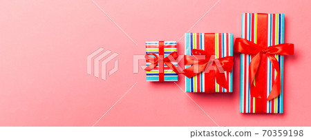wrapped Christmas or other holiday handmade present in paper with red ribbon on living coral background. Present box, decoration of gift on colored table, top view wrapped Christmas or other holiday handmade present in paper with red ribbon on living coral background. Present box, decoration of gift on colored table, top view 70359198