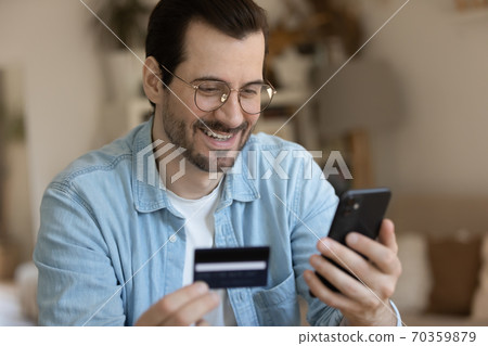 Young smiling man involved in online shopping in mobile app. Young smiling man involved in online shopping in mobile app. 70359879
