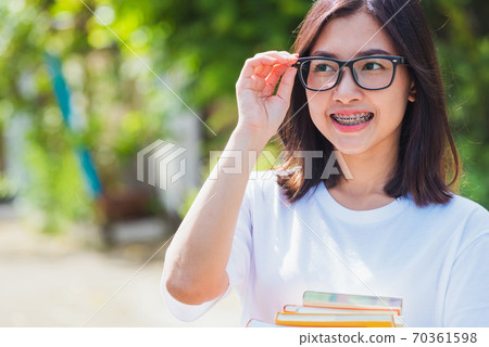 woman wear eyeglasses smile have dental braces on teeth laughing at outdoor she hold education books on hand 70361598