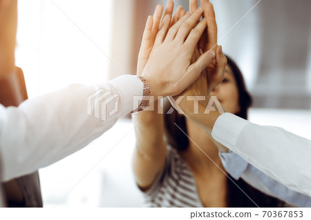 Group of business people joining hands or giving five to each other after meeting or negotiation in sunny office Group of business people joining hands or giving five to each other after meeting or negotiation in sunny office 70367853