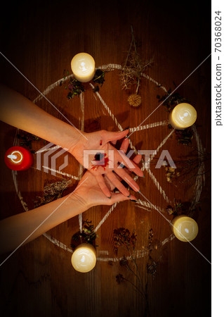 Female bleeding hands on the altar in the dark. Witch carry out a black magic ritual using her own blood, pentagram, candles, dry herbs on wooden surface, low key, vertical photo, selected focus. 70368024